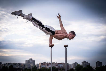 Flexible acrobat doing handstand on the cityscape background with dramatic clouds. Concept of willpower, control and dreamの写真素材