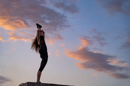 Flexible female dancer on the edge of rooftop on the dramatic sky background during sunset . Concept of healthy lifestyle, talent and aspirationの写真素材