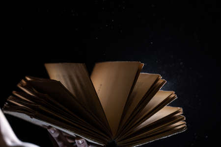 Hand holds Vintage open Book Glows on black background. Concept of reading, knowledge and open mindの写真素材