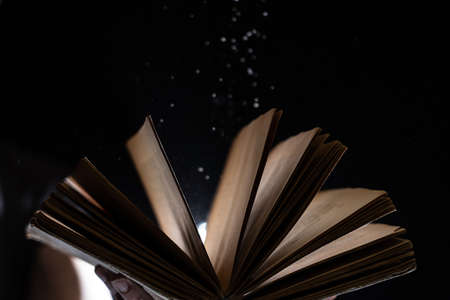Hand holds Vintage open Book Glows on black background. Concept of reading, knowledge and open mindの写真素材