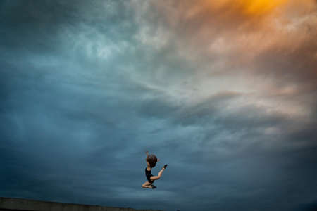Super flexible woman jumping on the sky background. Concept of healthy lifestyle, talent and aspirationの写真素材