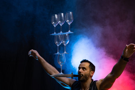 Man hold knife in the mouth and keep in balance wineglasses on it. concentrationの写真素材