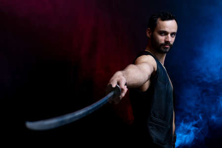 Muscular Man posing with long sword isolated on black and smoked backgroundの写真素材