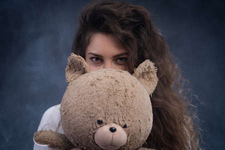 cheerful curly young woman holding teddy bear. concept of present and happinessの写真素材