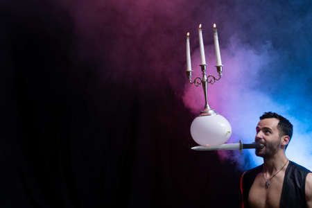 A circus artist holds a knife in his mouth a balloon with a candelabrum and burning candles on it and keeps it in balanceの写真素材