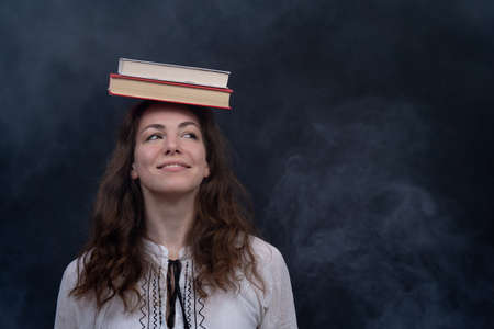 Girl holding books on the head. Concept of genius, meditation and knowledgeの写真素材