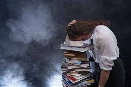 Sad female student reading with lots of books for the exam. Concept homeschoolingの写真素材