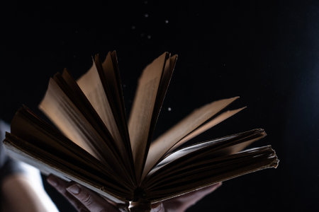 Hand holds Vintage open Book Glows on black background. Concept of reading, knowledge and open mindの写真素材