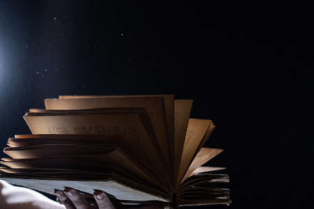 Hand holds Vintage open Book Glows on black background. Concept of reading, knowledge and open mindの写真素材