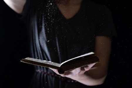 Hands hold Vintage open Book Glows on black background. Concept of reading, knowledge and open mindの写真素材