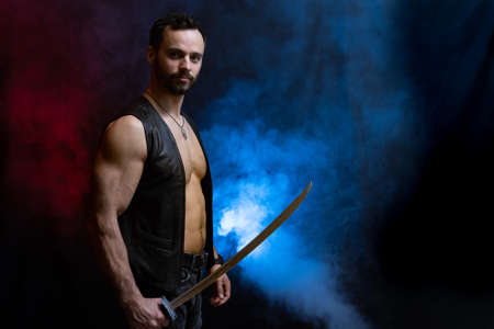 Muscular Man posing with long sword isolated on black and smoked backgroundの写真素材