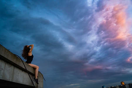Silhouette of woman sitting on the edge of rooftop on the dramatic sky background during sunset. Concept of dream, chance and opportunity.の写真素材
