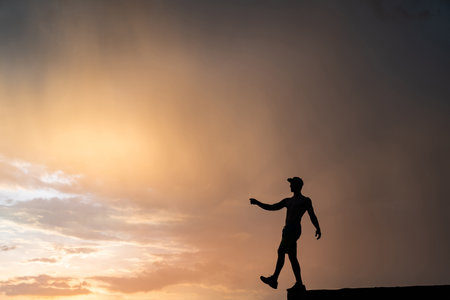 Muscular man stepping from the edge during dramatic sunset. Concept of choice and courageの写真素材