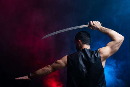 Muscular Man posing with long sword isolated on black and smoked backgroundの写真素材