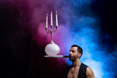 A circus artist holds a knife in his mouth a balloon with a candelabrum and burning candles on it and keeps it in balanceの写真素材