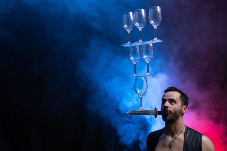 Man hold knife in the mouth and keep in balance wineglasses on it. concentrationの写真素材