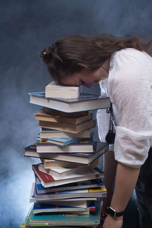 Sad female student reading with lots of books for the exam. Concept home education.の写真素材