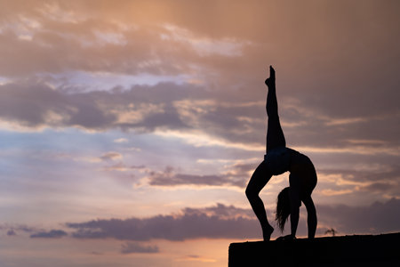 Flexible girl doing exercise on sky background during dramatic sunsetの写真素材