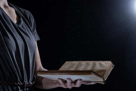 Hands hold Vintage open Book Glows on black background. Concept of reading, knowledge and open mindの写真素材