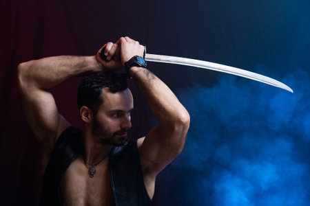 Muscular Man posing with long sword isolated on black and smoked backgroundの写真素材