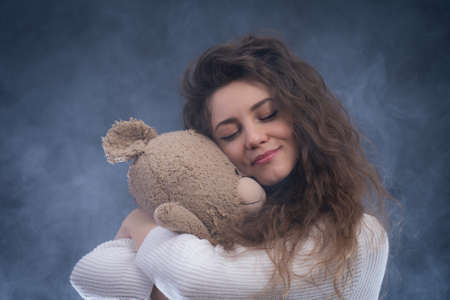 cheerful curly young woman holding teddy bear. concept of present and happinessの写真素材
