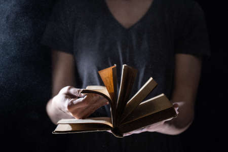 Hands hold Vintage open Book Glows on black background. Concept of reading, knowledge and open mindの写真素材
