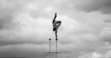 Circus artist keeps balance on one hand on the cloudy sky background. Concept of handstand, performing and artの写真素材