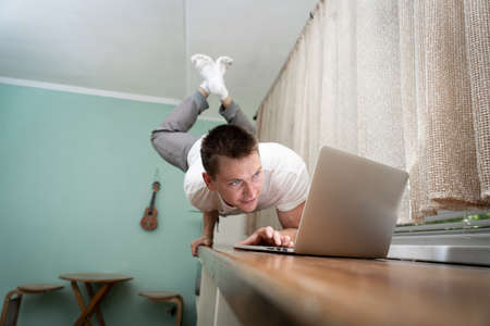 A muscular man practice yoga on one hand and works at a laptop. Self-isolation, remote working and healthy lifestyle conceptの写真素材
