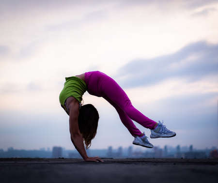 Flexible woman doing handstand outdoor on the dramatic sunset background. Concept of yoga, healthy lifestyle and individualityの写真素材