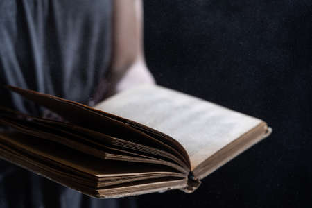 Hands hold Vintage open Book Glows on black background. Concept of reading, knowledge and open mindの写真素材
