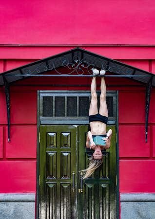 Girl hanging by feet upside down in the street and reading book. Concept of education and self-developmentの写真素材