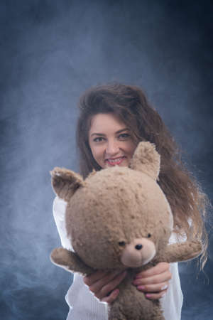 cheerful curly young woman holding teddy bear. concept of present and happinessの写真素材