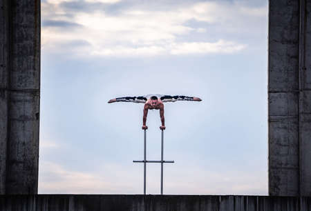 Flexible male circus Artist keep balance on hands in the concrete structure on sky background with reflection in the water. Equality, consistency and symmetry concept.の写真素材