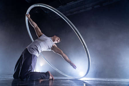 Cyr Wheel circus artist on smoked, dark background performing on stageの写真素材