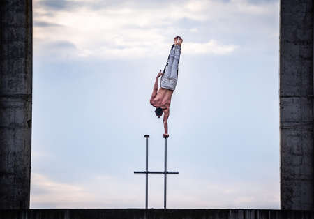Circus artist keeps balance on one hand on the sky and industrial construction background. Concept of handstand, performing and artの写真素材