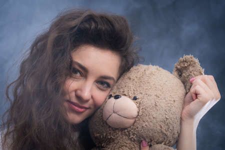 cheerful curly young woman holding teddy bear. concept of present and happinessの写真素材