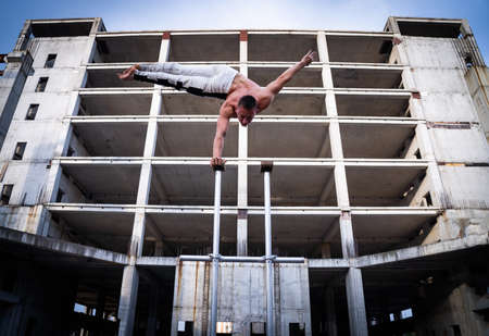 Flexible acrobat doing handstand on the industrial construction background with columns on sides. Concept of willpower, control and dreamの写真素材