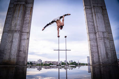 Circus artist keeps balance on one hand on the sky and industrial construction background. Concept of handstand, performing and artの写真素材