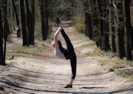 Flexible female gymnast makes exercise in the forest. Healthy lifestyleの写真素材