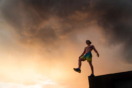 Muscular man stepping from the edge during dramatic sunset. Concept of choice and courageの写真素材