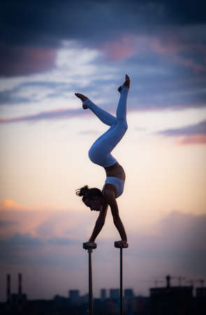 Flexible female circus Artis keep balance and doing contortion on the rooftop against dramatic sunset and cityscape. Motivation, passion and achievement conceptの写真素材
