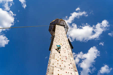 Sportsman climber training outdoor with blue sky , climbing on artificial colourful rock wall. Healthy lifestyle and bouldering concept.の写真素材