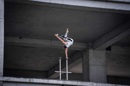 Circus artist keeps balance on one hand in the industrial concrete structures background. Concept of handstand, performing and artの写真素材