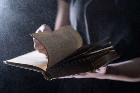 Hands hold Vintage open Book Glows on black background. Concept of mystery, riddle and secretの写真素材