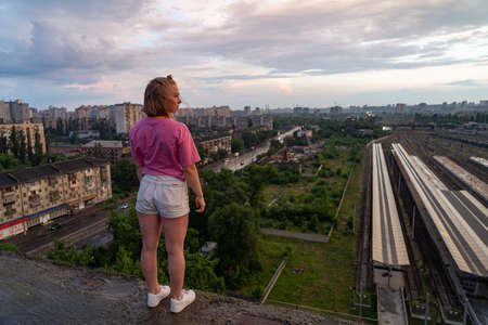 Young woman standing on a rooftop and looking at the cityscape with dramatic skyの写真素材