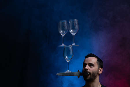 Man hold knife in the mouth and keep in balance wineglasses on it. concentrationの写真素材