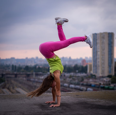 Flexible girl keep balance on hands on the cityscape background . Concept of creativity, balance and individualityの写真素材