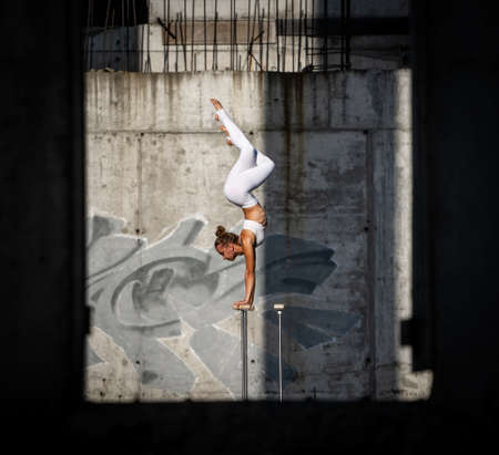 Flexible and fit girl standing on her hands keeping balance in the abandoned building. Concept of fitness, workout and motivationの写真素材