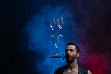 Man hold knife in the mouth and keep in balance wineglasses on it. concentrationの写真素材