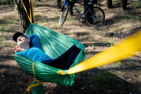 Young happy man in hat relaxing outside in hammock in forest.の写真素材